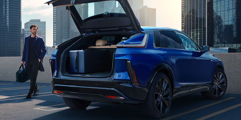 Blue Cadillac LYRIQ SUV with open trunk and a man walking nearby.