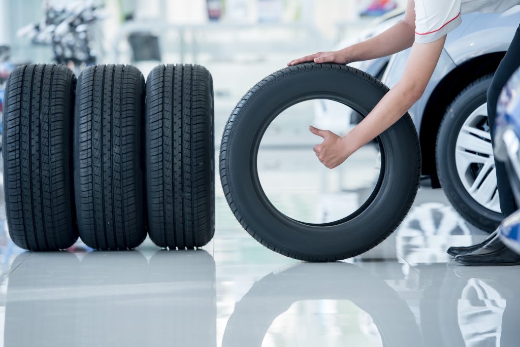 Person holding a tire in a showroom next to stacked tires, giving a thumbs-up.