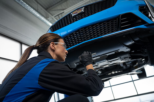 Automotive technician inspecting the underside of a blue vehicle on a lift during a service inspection.