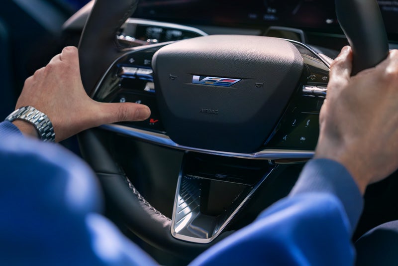 Close-up of a Man About to Press the V-Button on the 2026 OPTIQ-V Steering Wheel | Mitch Hall Cadillac in Lamesa TX