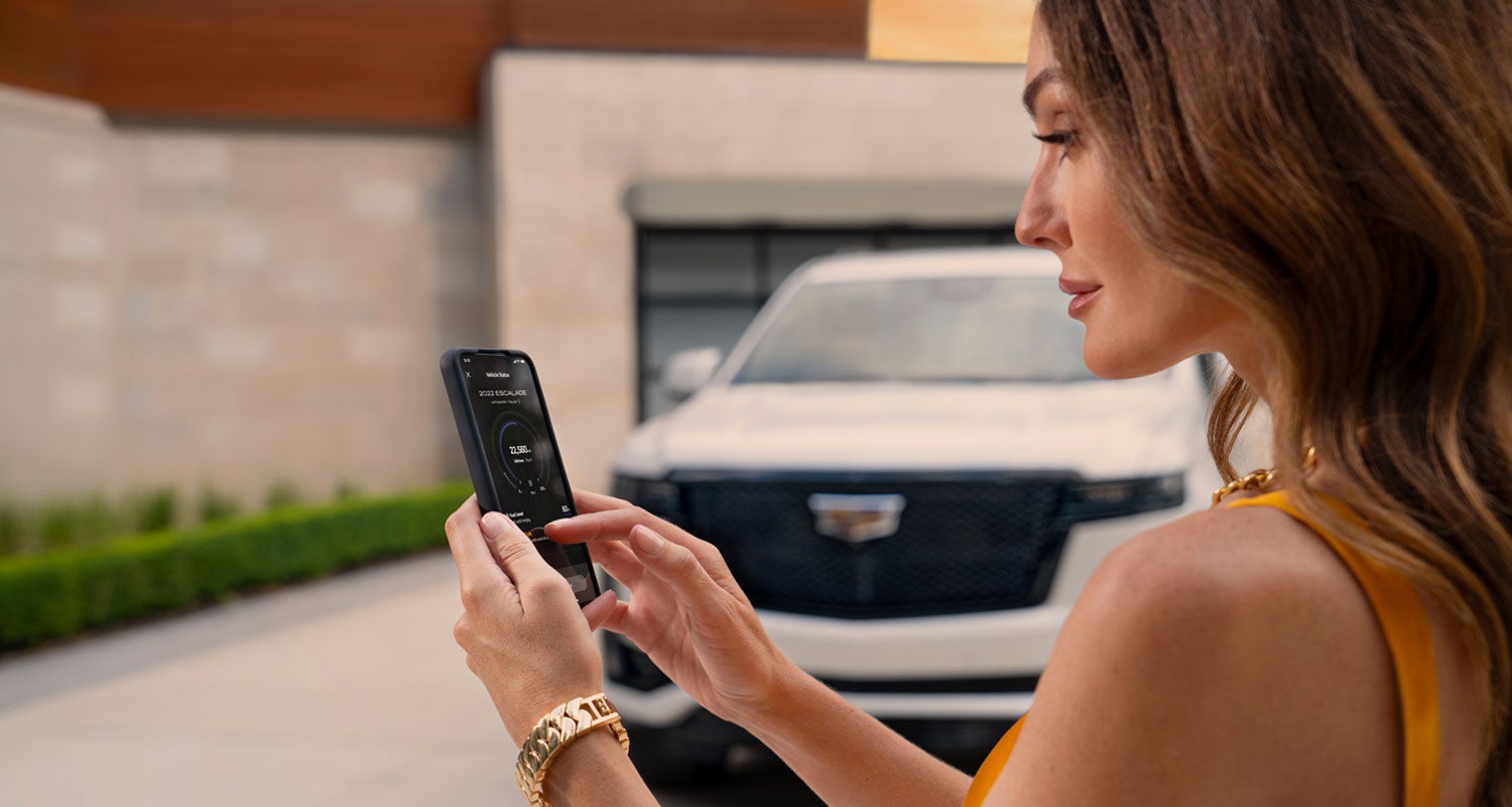 lady checking her mobile with a Cadillac vehicle background | Mitch Hall Cadillac in Lamesa TX